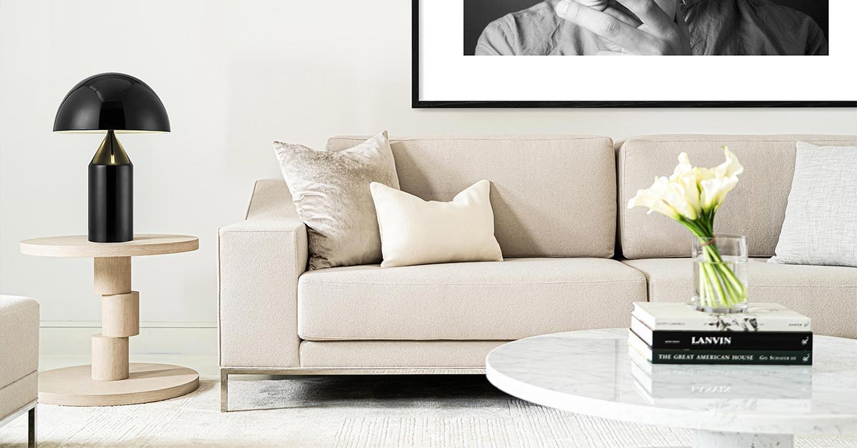 The Domicile New Edition collection designed by Michael Vanderbyl for Decca. The image depicts a modern Scandinavian-style interior with a white upholstered sofa, a round marble dining table and a light brown widen slide table with a black table lamp on top.