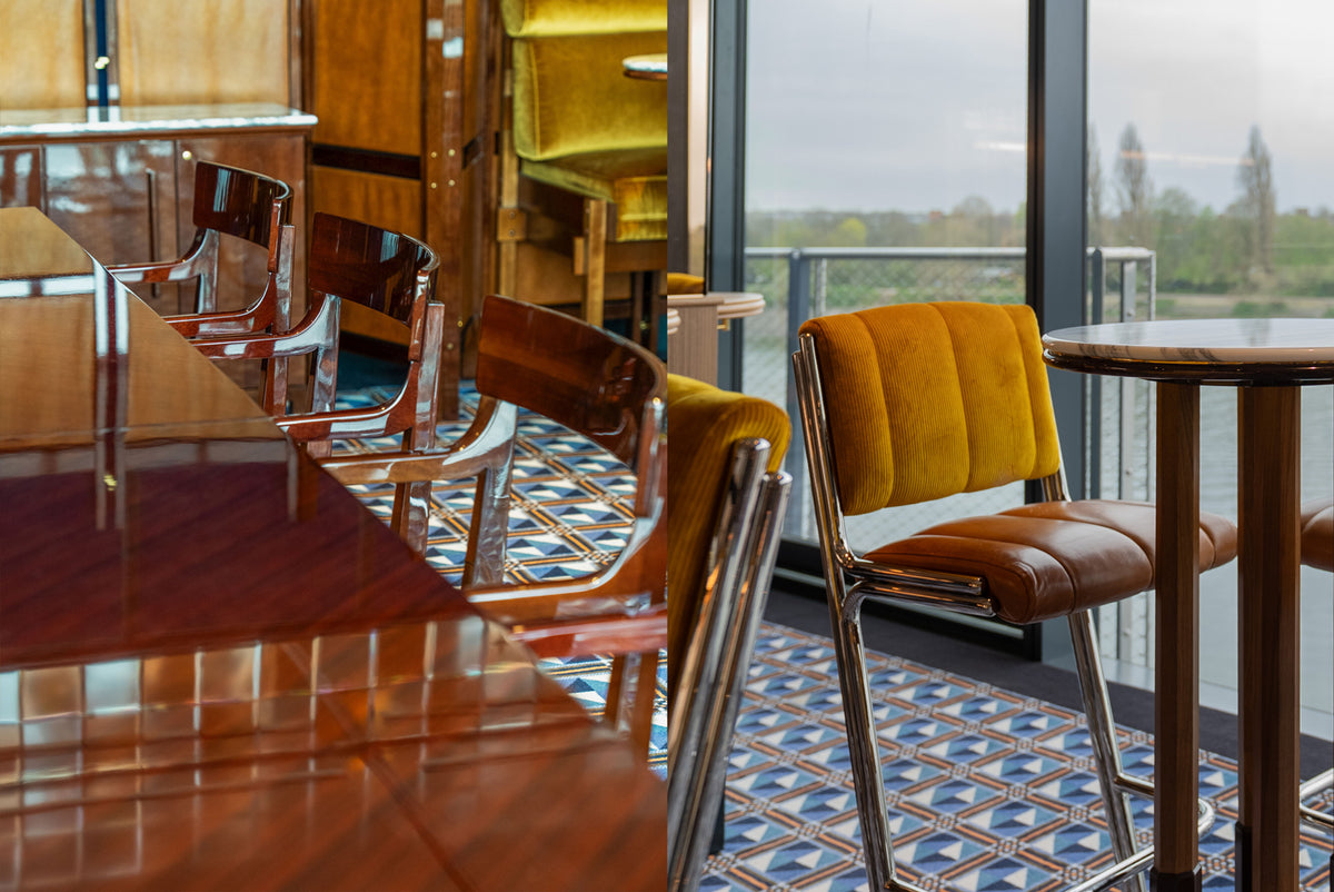 A modern interior with a large wooden table and chairs. Yellow velvet upholstered chairs, brown leather seating, and a large window overlooking water and trees.