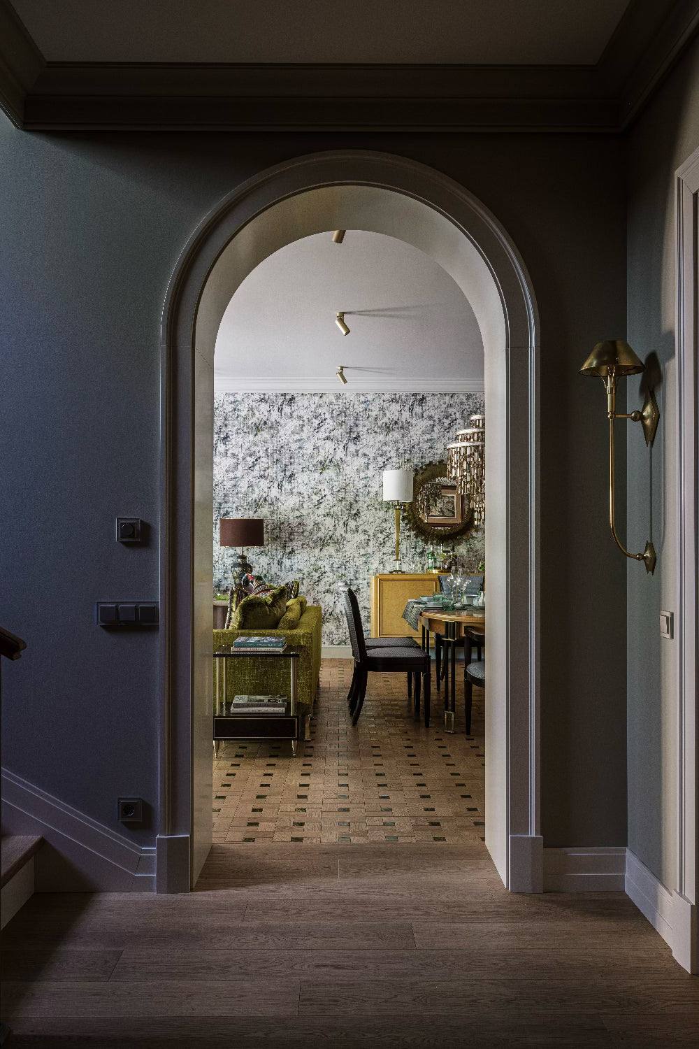 Passageway leading to a dining and living room with floral wallpaper and furniture, including green upholstered sofas.
