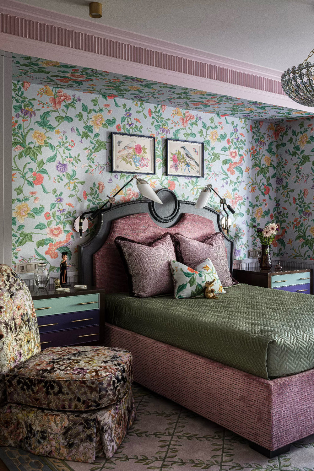 Decorative bedroom with floral wallpaper, pink upholstered bed, and patterned upholstered armchair.
