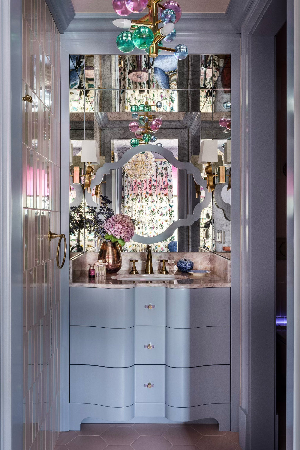 Luxurious bathroom with a colourful pendant light, mirrors, and decorative elements including a vase with pink flowers.