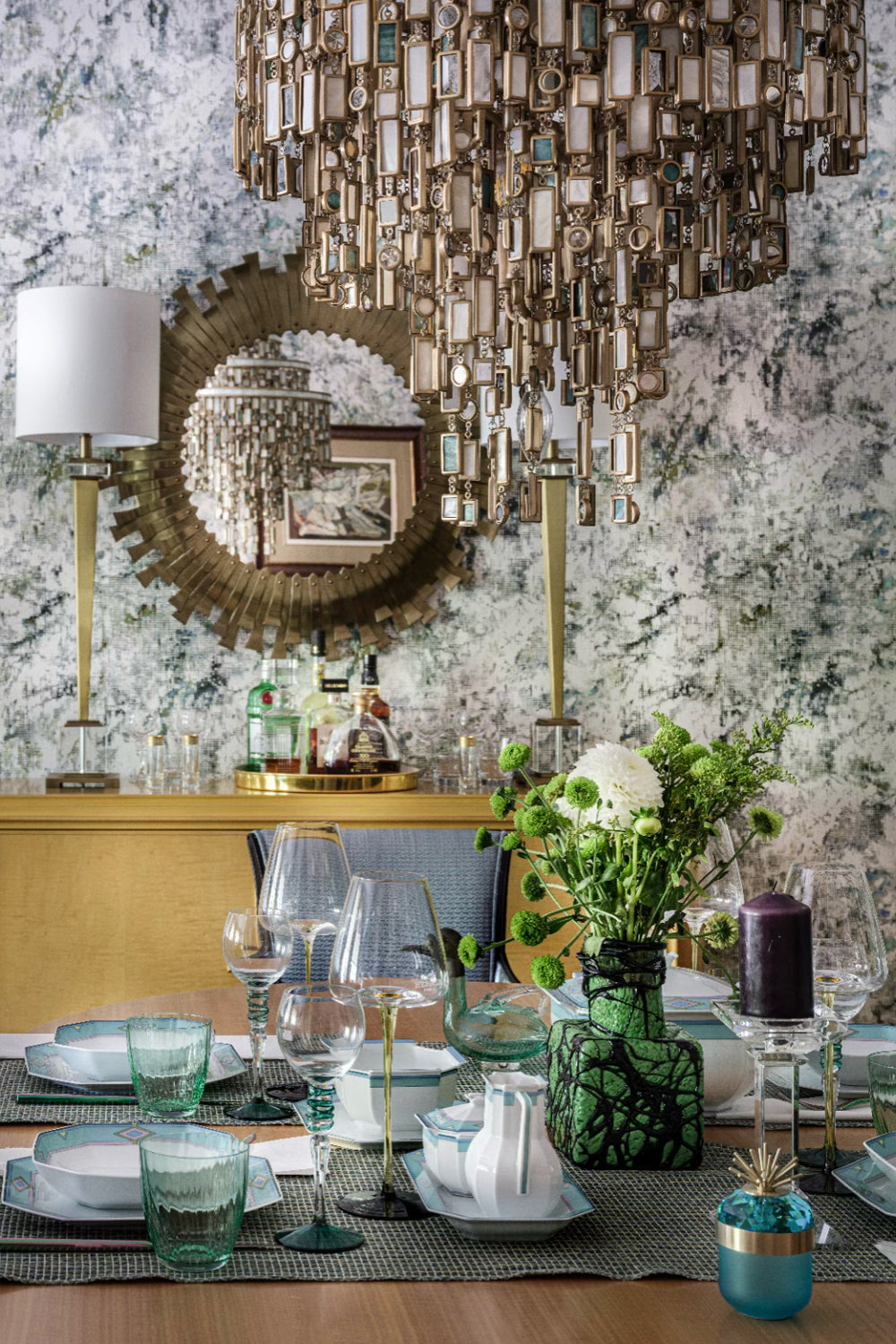 Dining room with a decorative chandelier, mirror, and table setting, a light brown sideboard stands against the back wall.