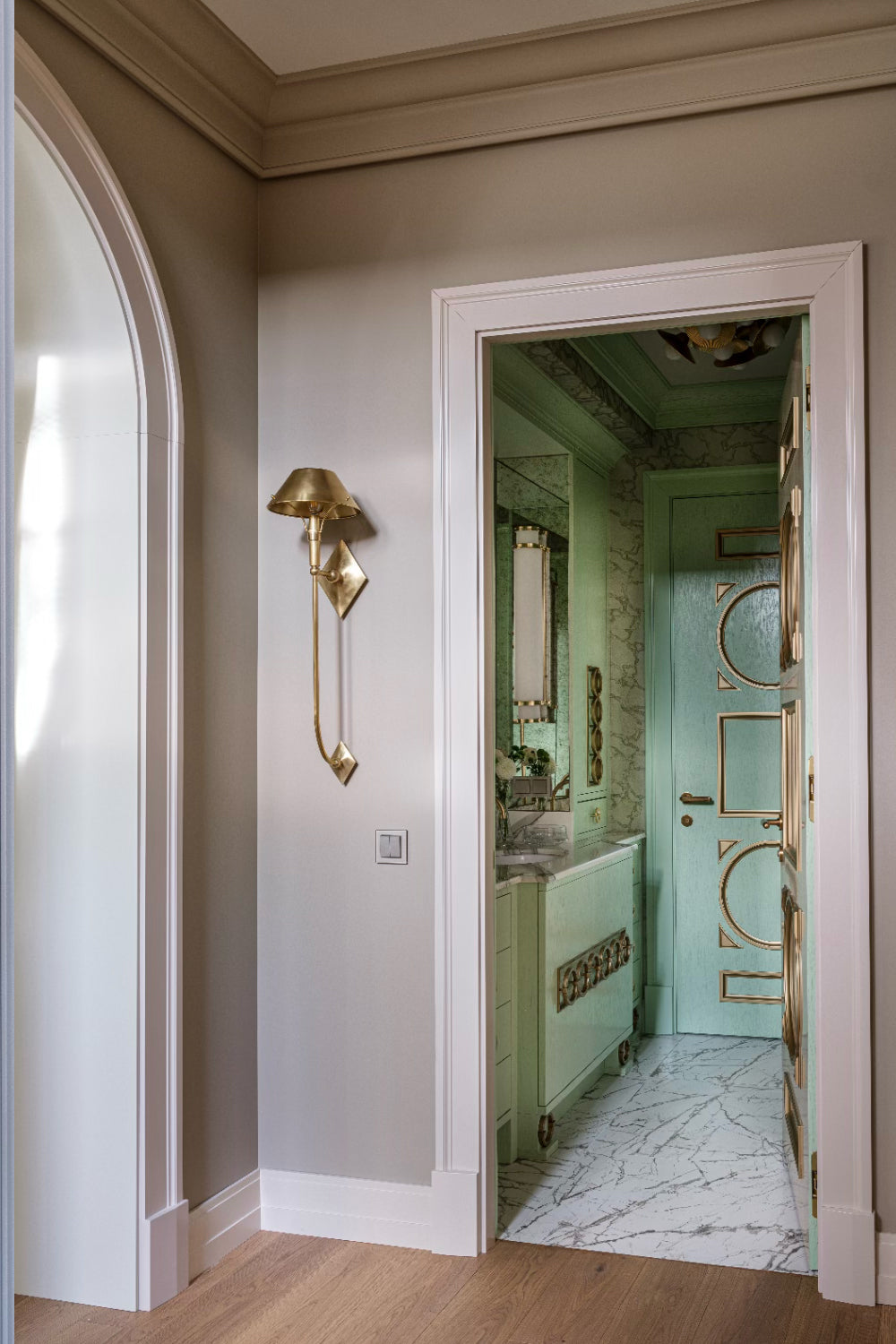 Hallway with a gold wall sconce and a door leading to a bathroom.