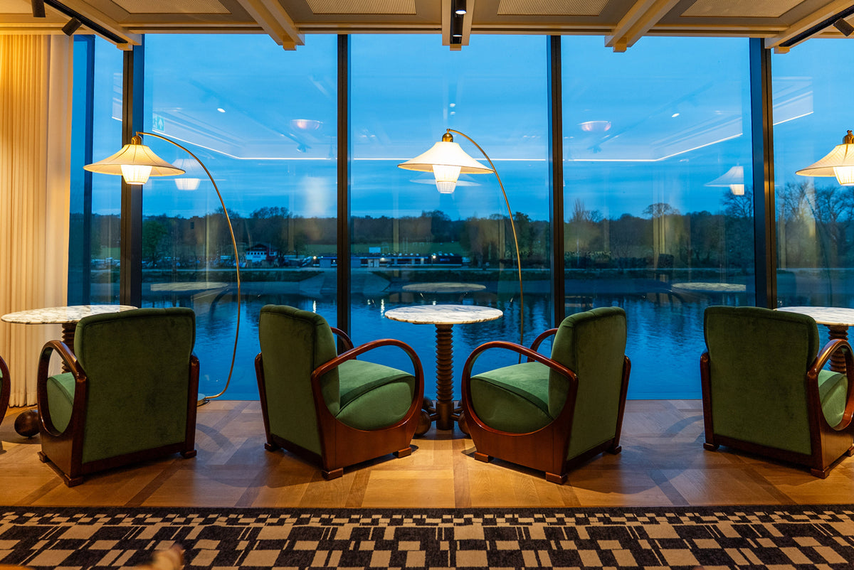 Modern interior with green chairs and round tables near large windows overlooking The Thames.